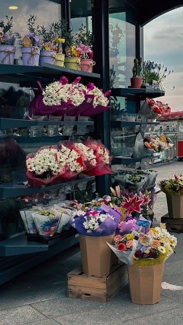 A display of various floral arrangements and bouquets showcased on dark blue tiered shelves and outdoor tables at a flower shop on Queensbury High Street. The arrangements include mixed fresh flowers 